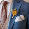 Dried flower buttonhole with a bright-orange strawflower, yellow and blue accents pinned to a blue grooms suit jacket.