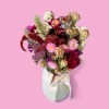 Close-up of a romantic dried flower bouquet in red, pink, white and beige tones against a pink background