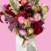 Close-up of a romantic dried flower bouquet featuring celosia, amaranthus, strawflower, statice and nigella in red, pink and cream tones against a pink background