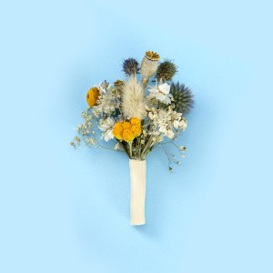 Dried flower buttonhole with yellow and blue blooms with white accents, wrapped with a white ribbon against a soft blue background