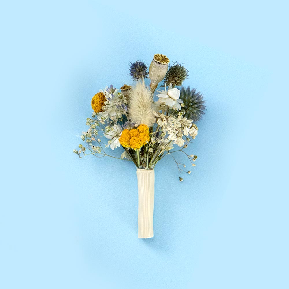 Dried flower buttonhole with yellow and blue blooms with white accents, wrapped with a white ribbon against a soft blue background