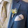 Dried flower buttonhole with White, yellow and blue flowers pinned to a blue grooms suit jacket.